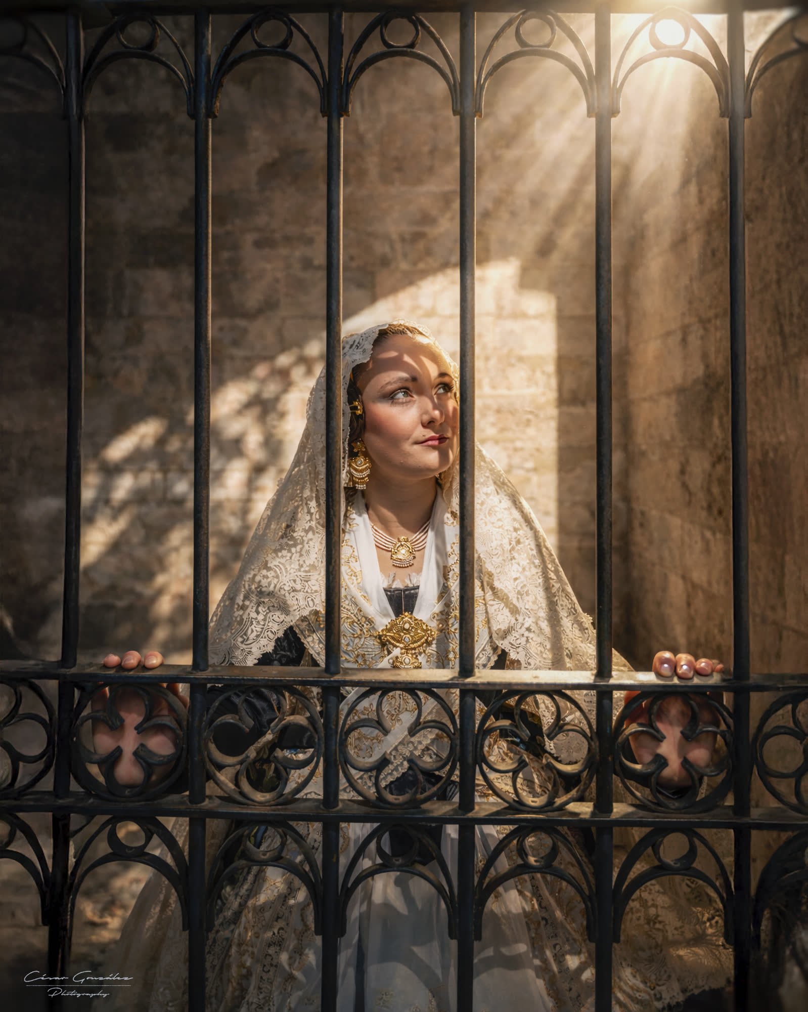 Fallera tras una reja de forja en Valencia, con la luz entrando por detrás — César González Photography